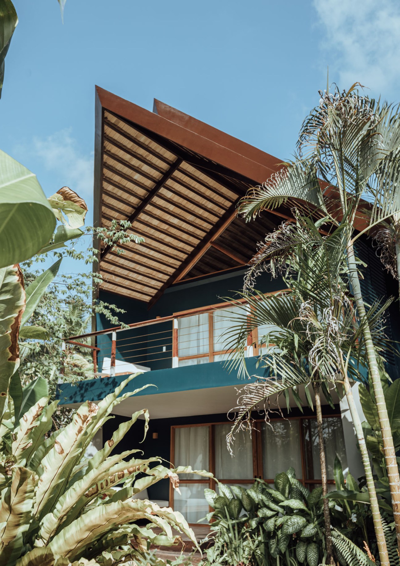 Modern tropical villa with distinctive bamboo roof overhang and lush palm vegetation