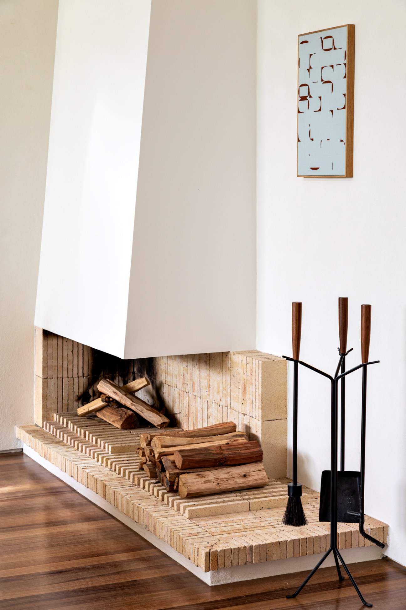 Modern white fireplace with cut-out geometric pattern, stacked firewood, and black fireplace tools