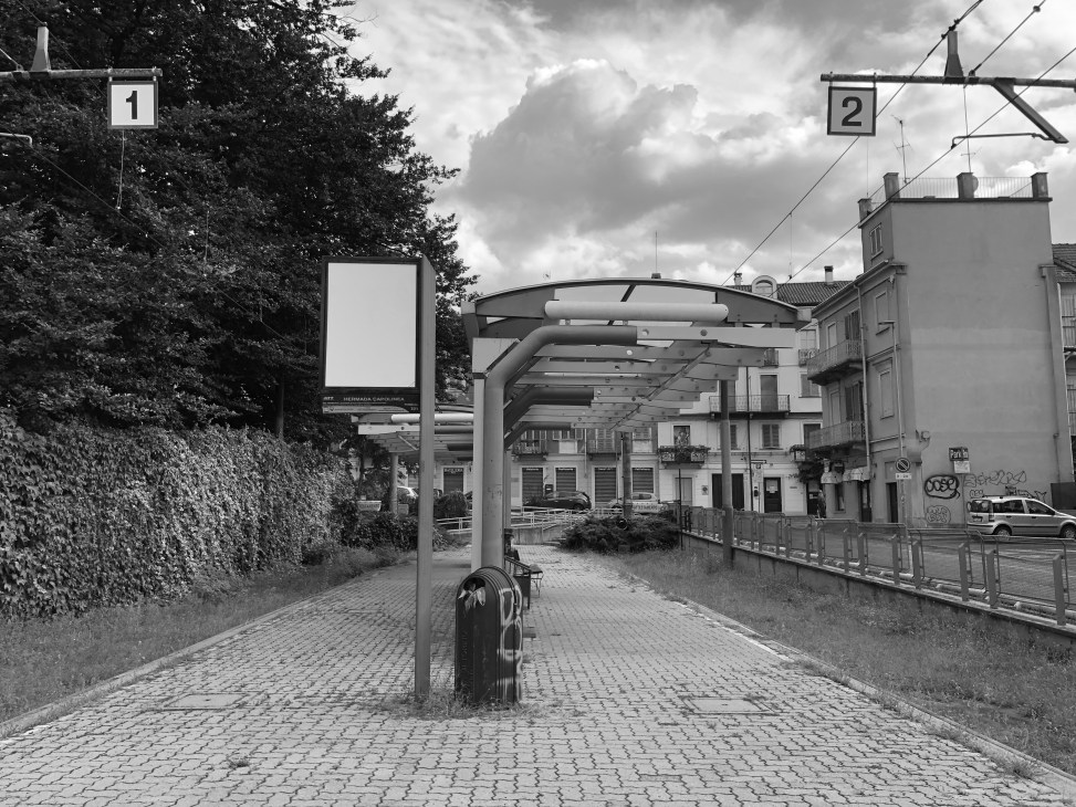 Black and white image of covered walkway with metal canopy over cobblestone platform and railway infrastructure