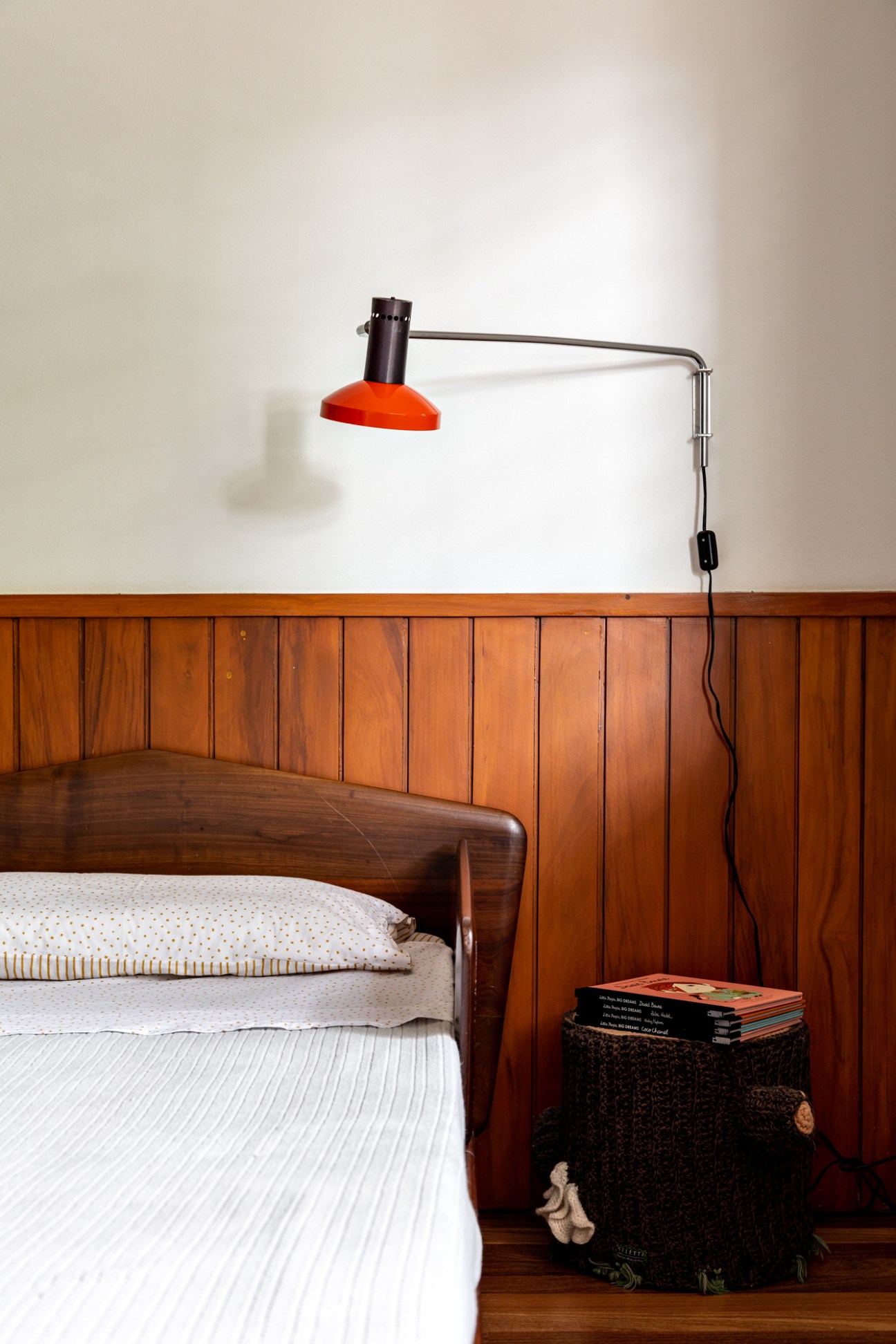 L'Atelier wall-mounted lamp with orange shade extending over bed with wooden headboard