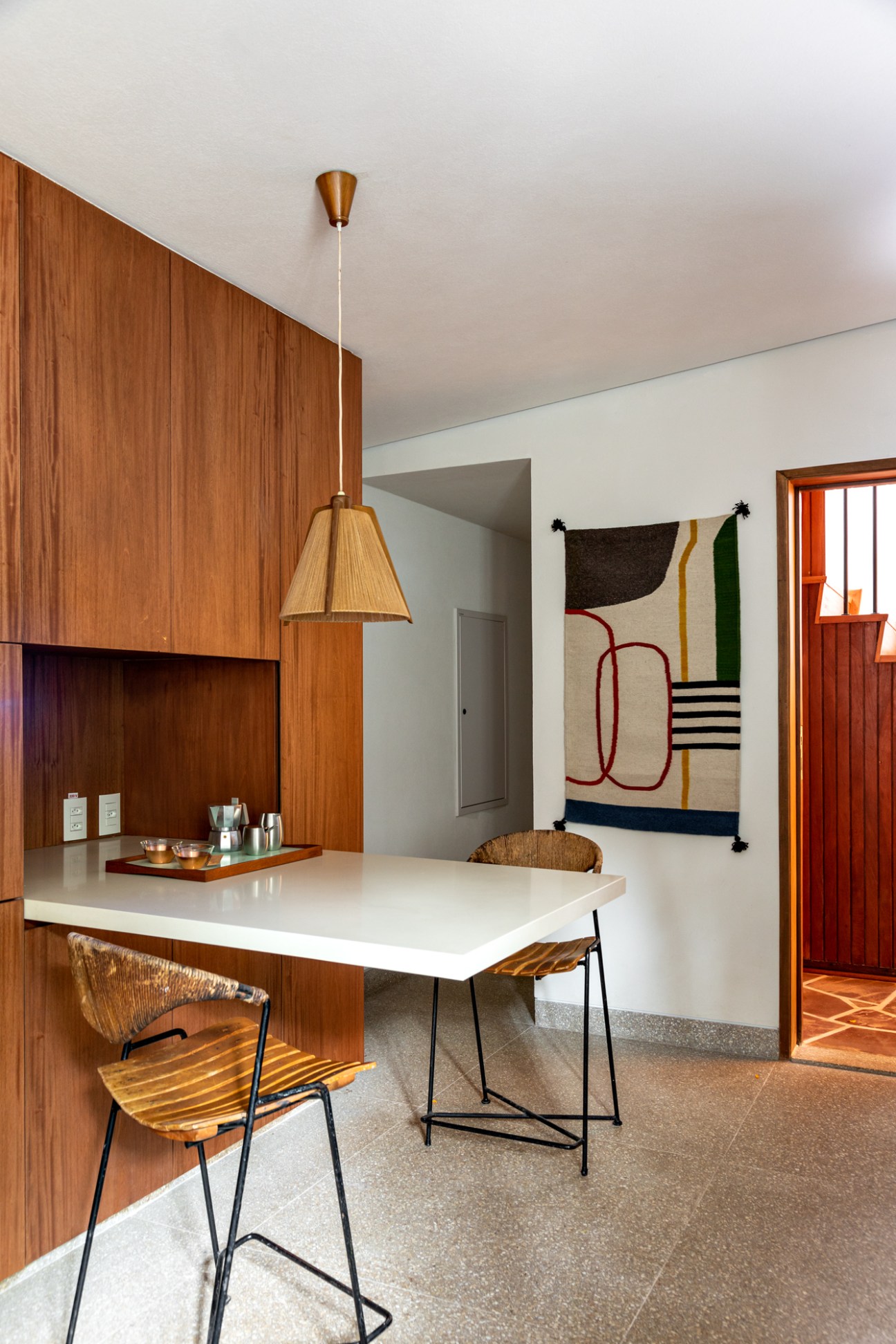 Modern kitchen with wood cabinetry, white countertop, woven bar stools and pendant light