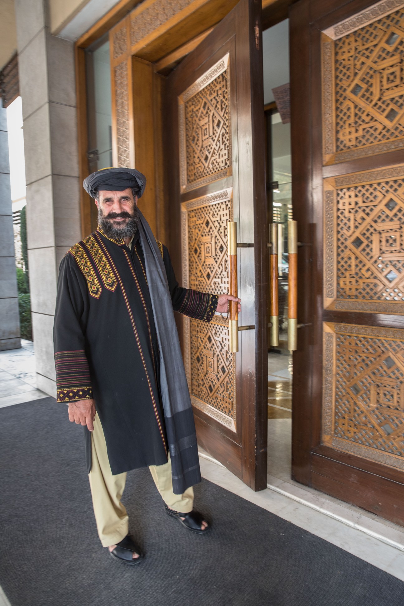 Hotel employee Haji Hazam in traditional Afghan dress standing by ornate wooden doors