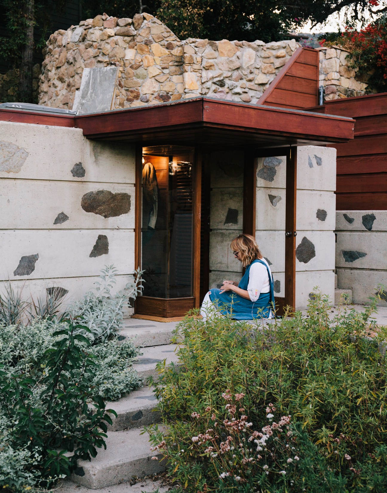 Woman in blue vest sitting outside modernist concrete and stone building with decorative aggregate panels.