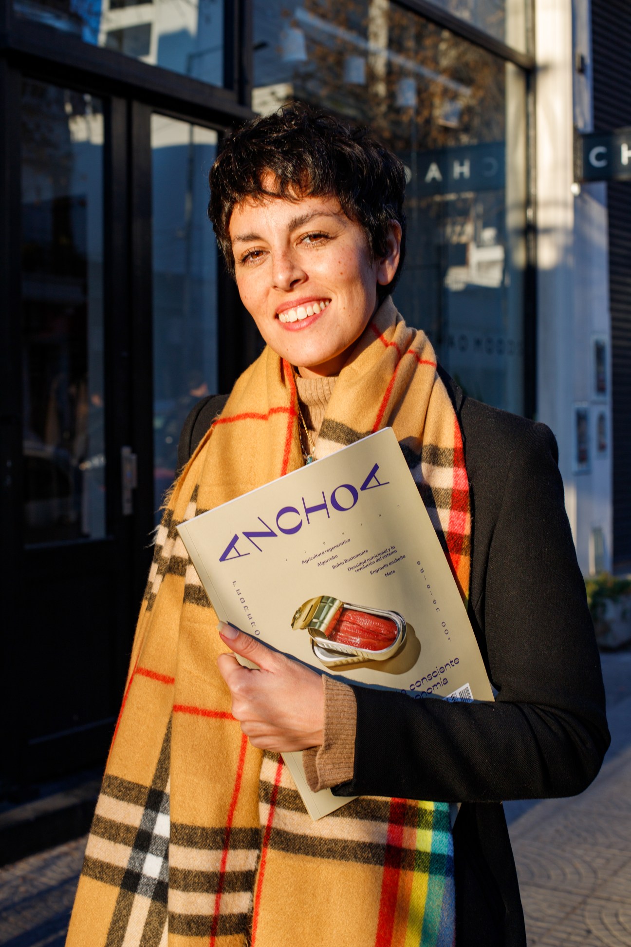 Woman holding Anchoa magazine while standing outdoors in sunlight