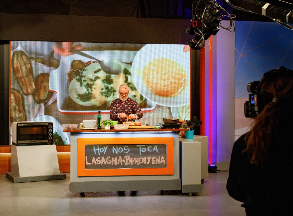 Chef cooking live on set at Canal de la Ciudad with recipe displayed on screen behind him.