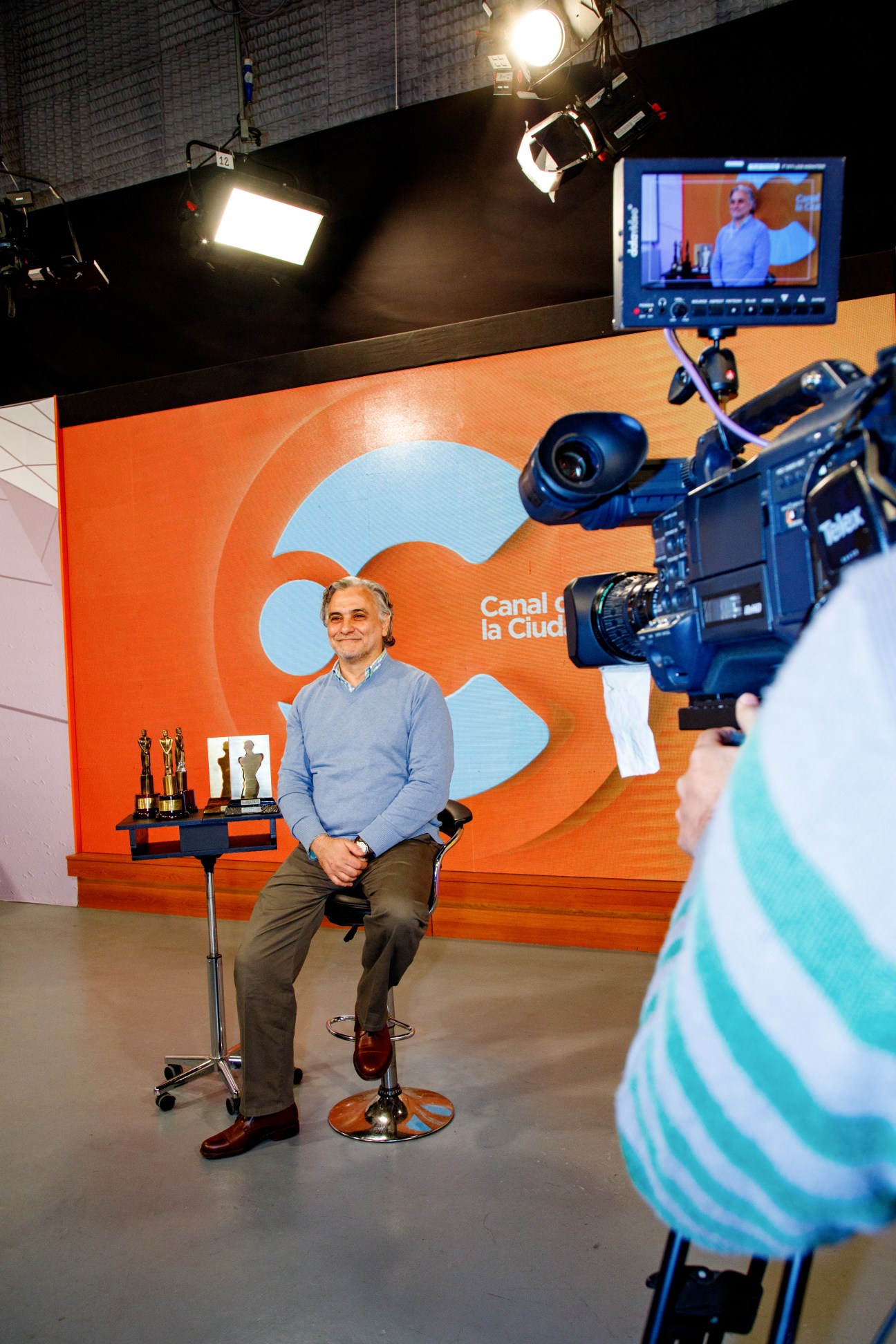 Eduardo Cura, director of Canal de la Ciudad, sits in a television studio set with professional lighting and camera equipment.