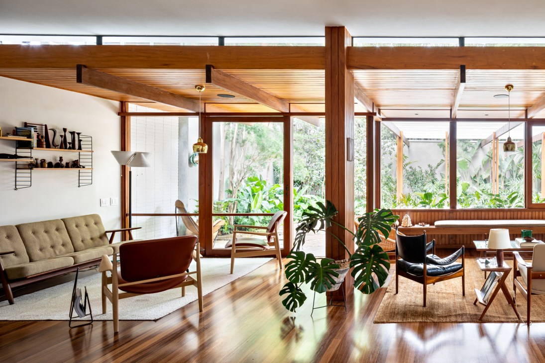Mid-century modern living room with wood beams, floor-to-ceiling windows, vintage furniture and tropical plants