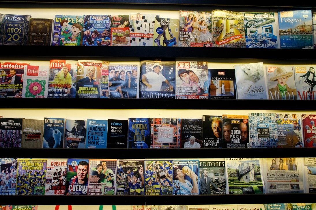 Shelves displaying various Spanish-language magazines and newspapers including Caras, Mía, and Clarín at Grupo Perfil's office.