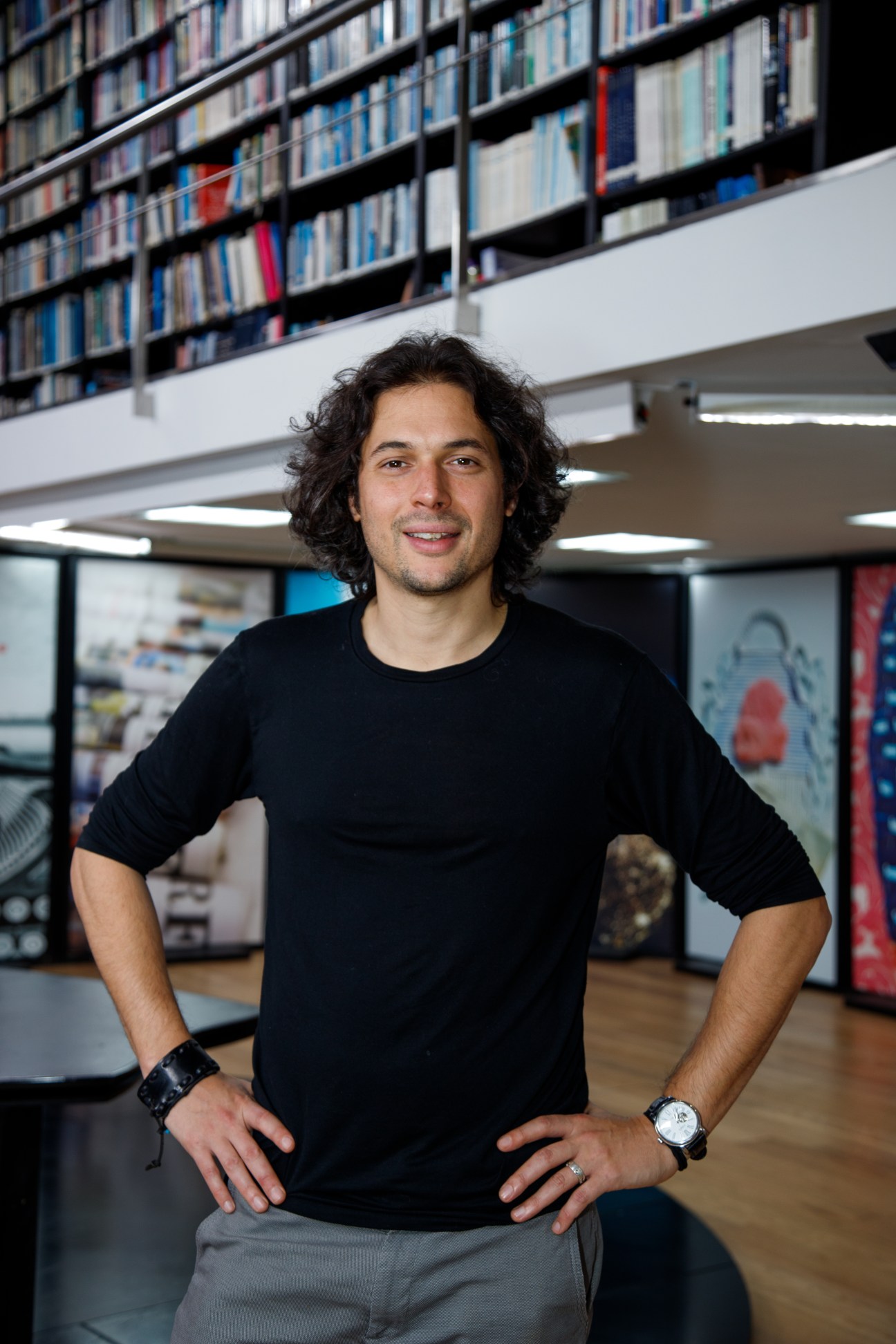 Man with dark curly hair standing in front of shelves of books and magazines in an office.