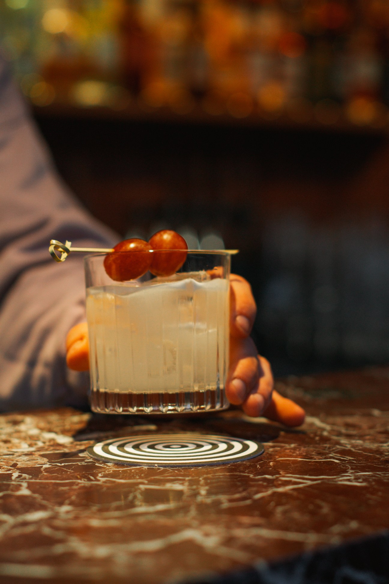 Hand holding cocktail glass with garnish on marble surface at Stereo bar