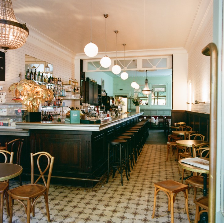 Interior of upscale restaurant with dark wood bar, pendant lighting, bentwood chairs and checkered floor tiles