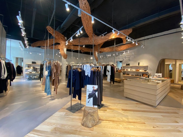 Interior of Adolfo Domínguez fashion store with wooden sculptural installations and displayed clothing on racks.