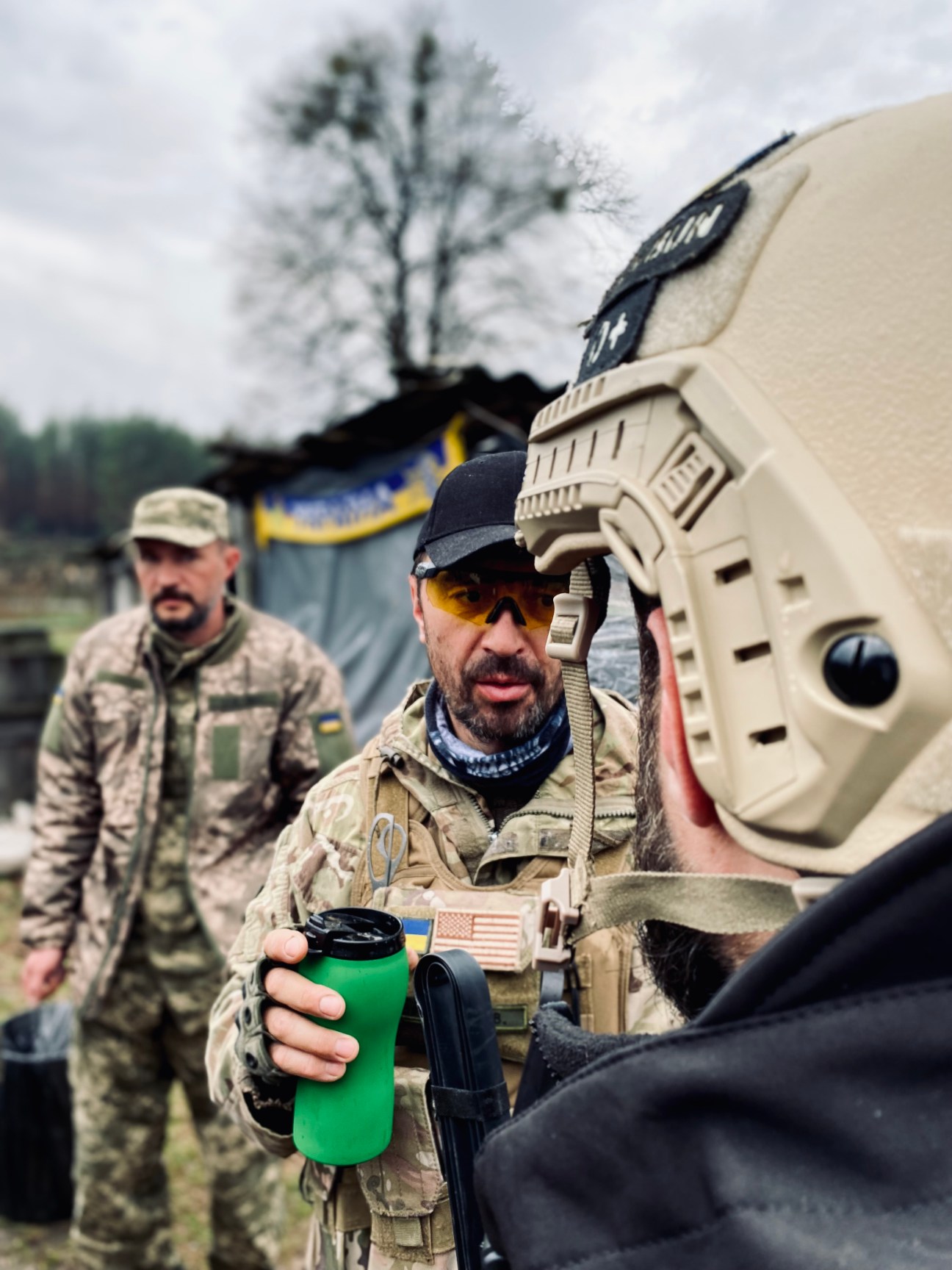 Two soldiers in military gear having a discussion, one holding a green cup