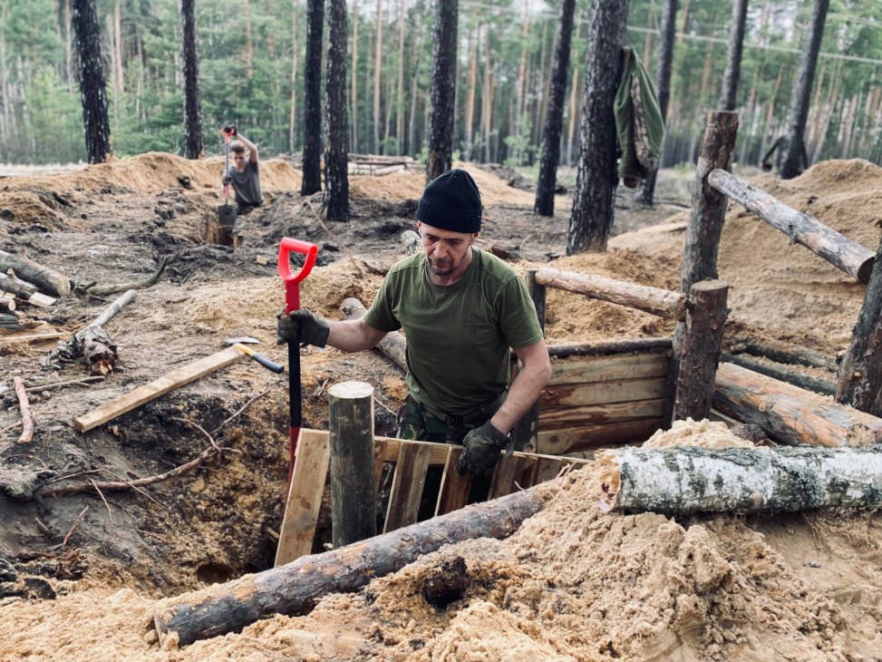 Soldier in military fatigues working in a wooden-reinforced trench in a forested area