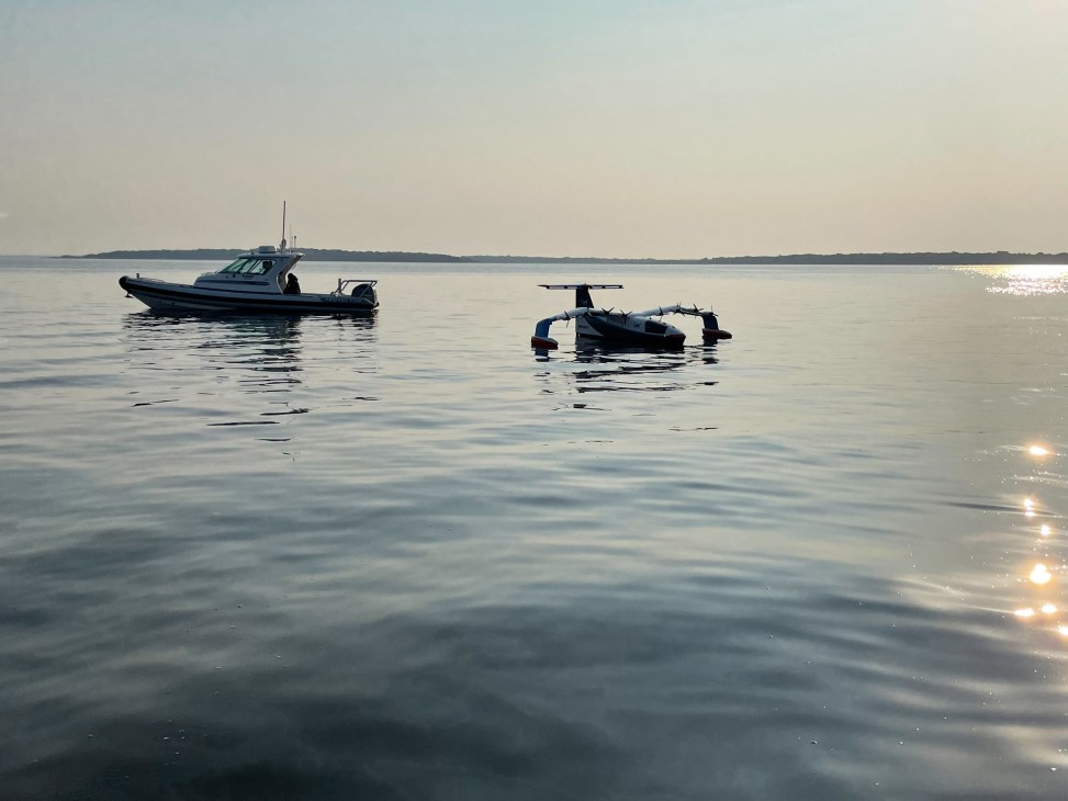 Two boats on calm water at dawn or dusk with sun reflecting on the surface and distant shoreline