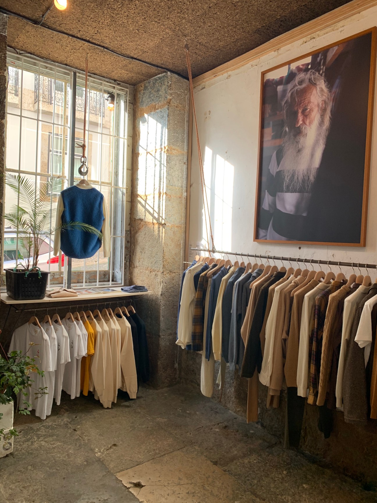 Interior of La Paz clothing store in Lisbon with hanging racks of neutral-toned garments and portrait on wall