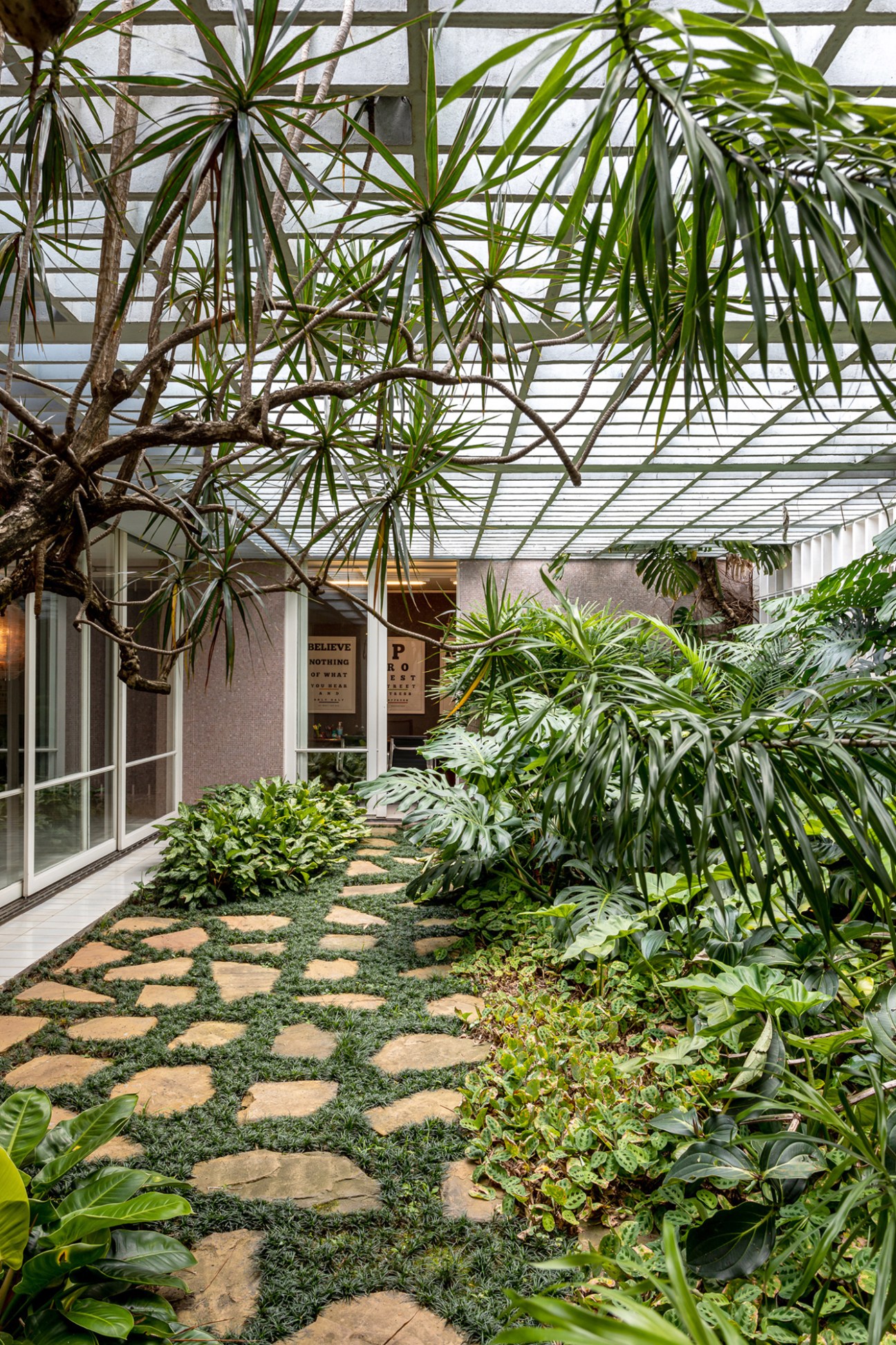 Indoor courtyard with lush tropical plants, stone pathway, and glass roof in modern residential building