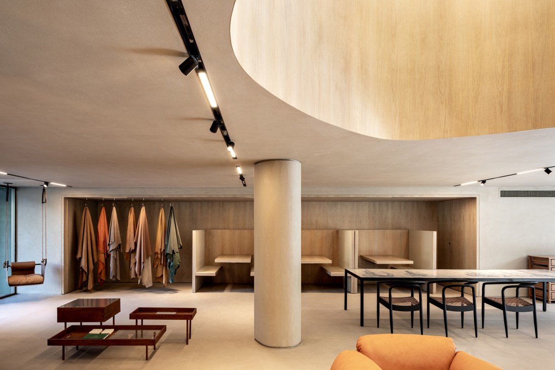Modern minimalist interior with curved wooden ceiling, cylindrical column, built-in seating nooks, and hanging fabric samples