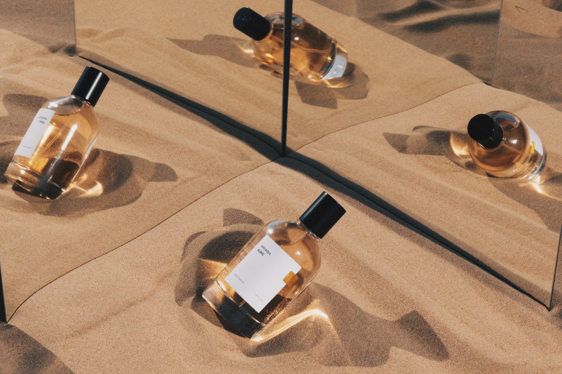 Arcadia perfume bottles with golden liquid arranged on sand with dramatic shadows in sunlight.