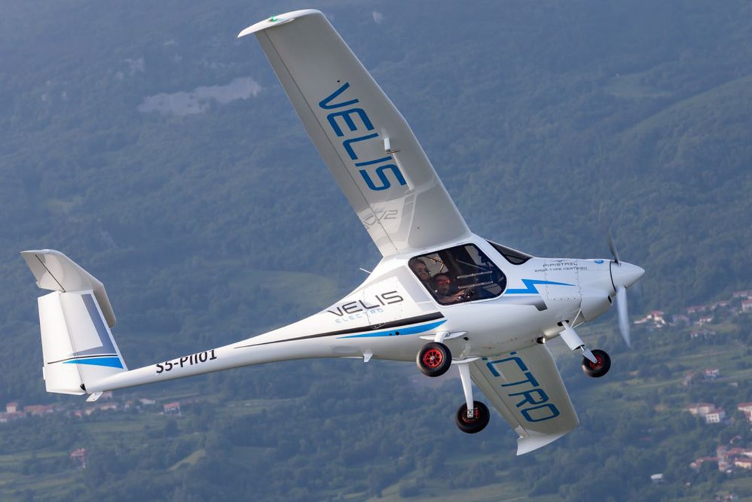 White Pipistrel Velis Electro aircraft in flight over mountainous landscape