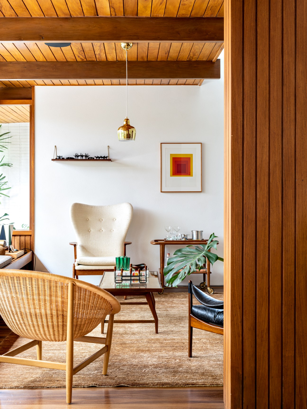 Mid-century modern living room with exposed wood ceiling beams, cream armchair, and brass pendant light