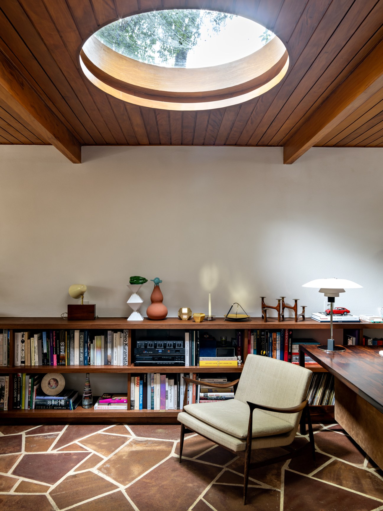 Study room with circular skylight, built-in bookshelves, chair and desk with warm wood ceiling