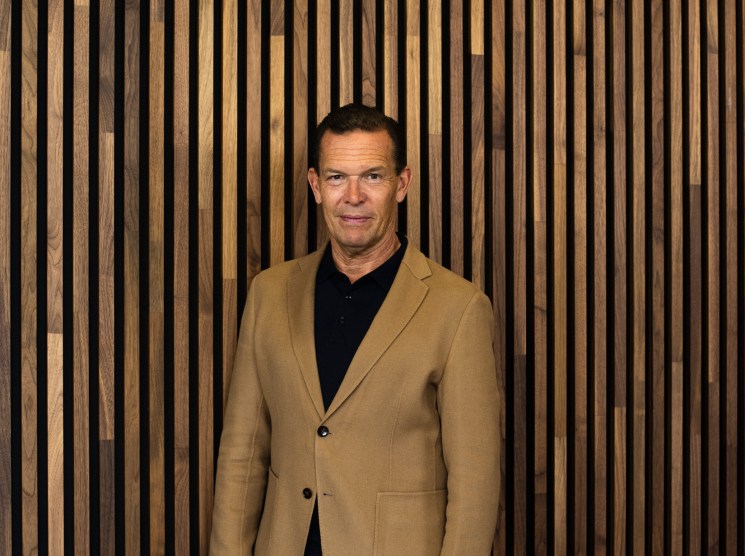 Daniel Grieder, CEO of Hugo Boss, wearing a camel blazer and black shirt against a wooden slat backdrop.