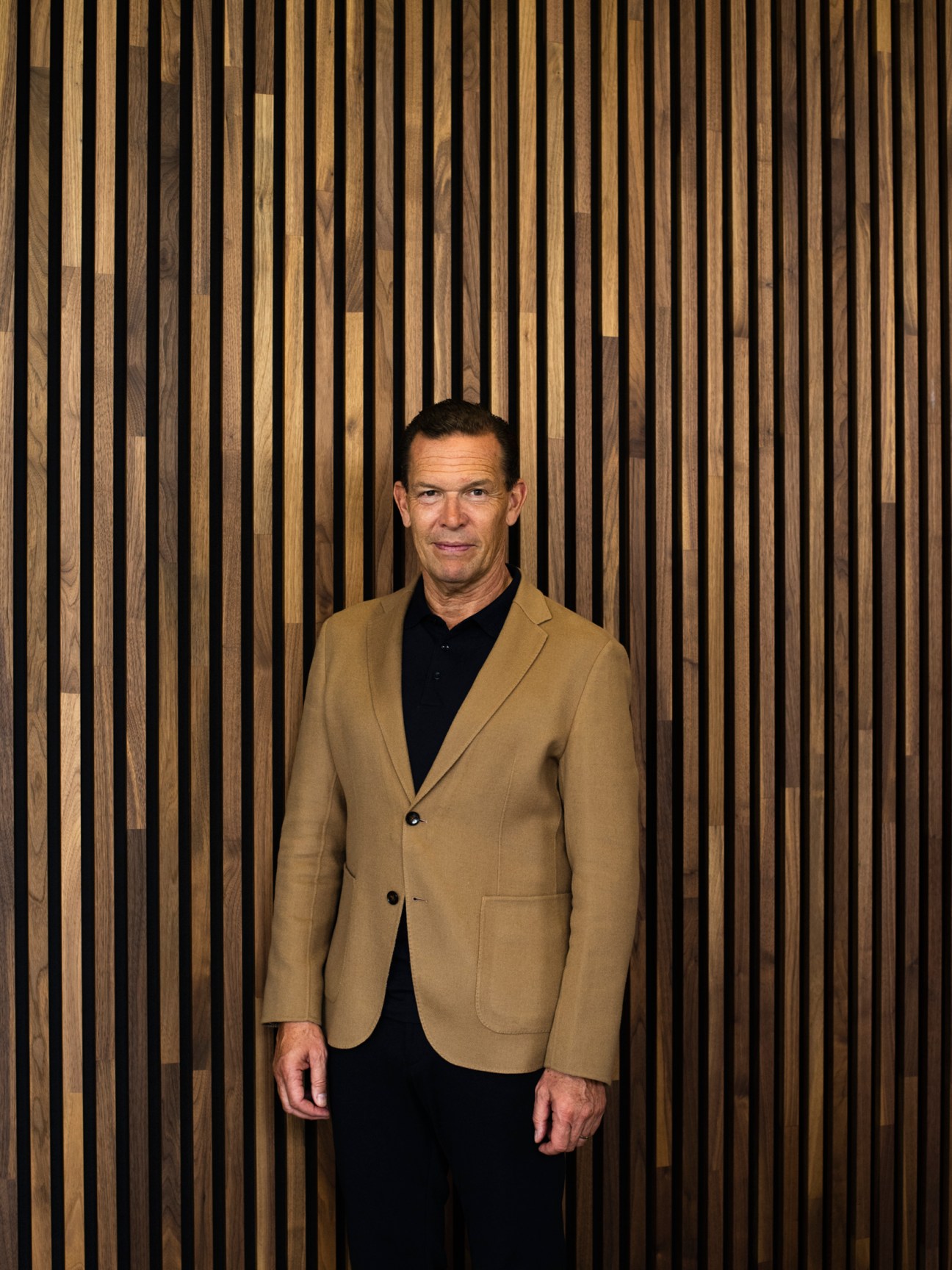 Daniel Grieder, CEO of Hugo Boss, wearing a camel blazer and black shirt against a wooden slat backdrop.