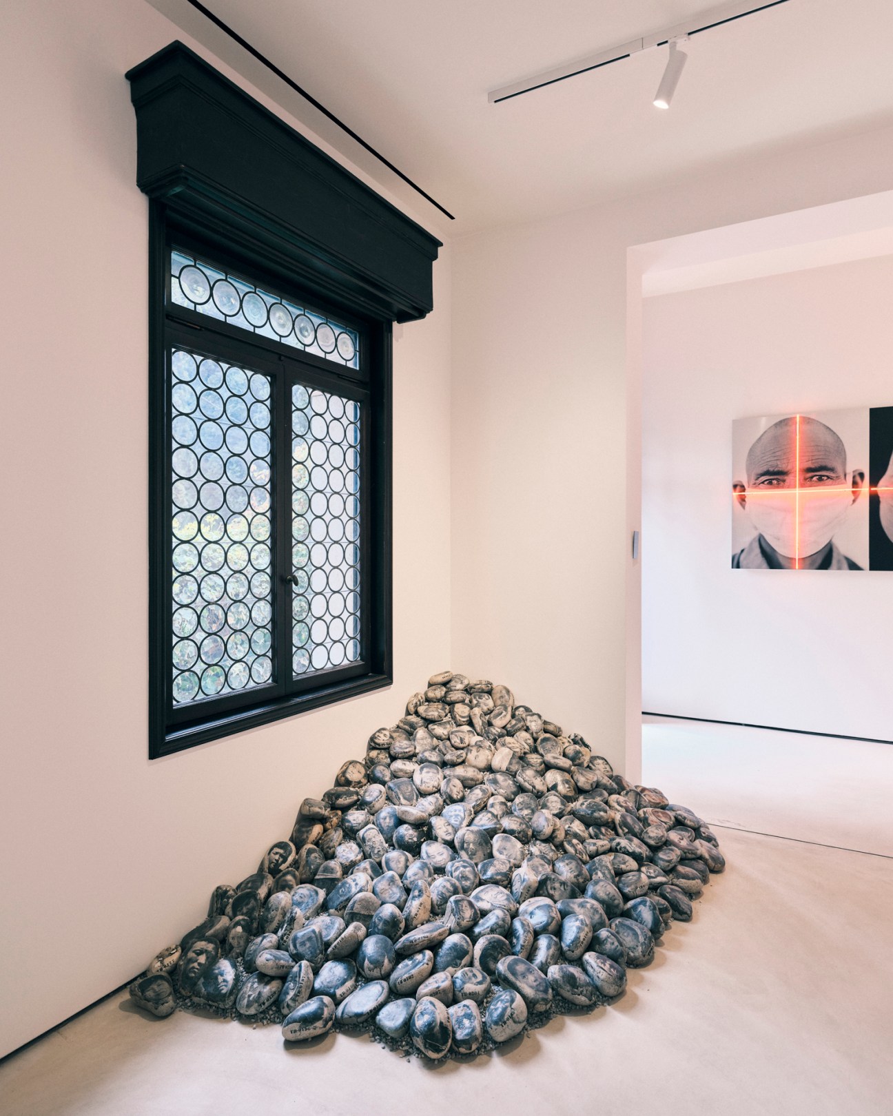 Gallery interior displaying a sculptural installation of stacked oyster shells below a black-framed window, with a portrait visible on the right wall.
