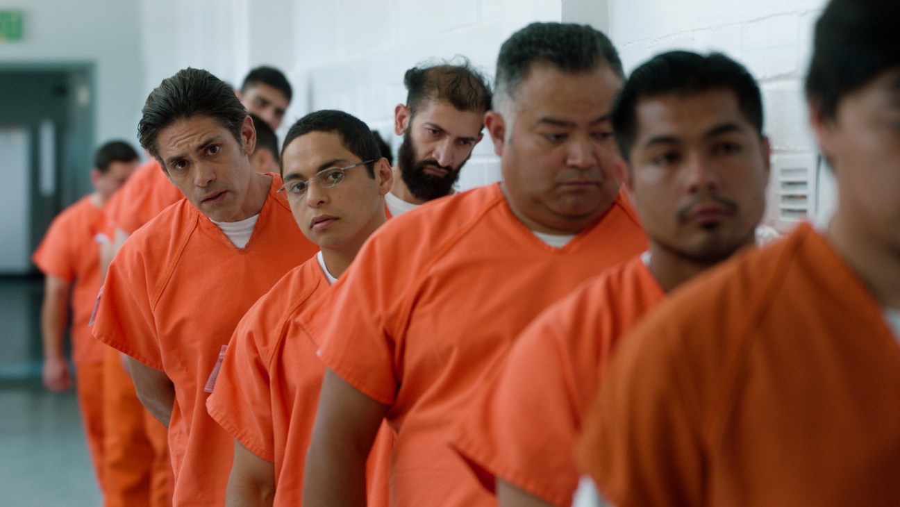 Men in orange prison uniforms stand in a line inside a detention facility.