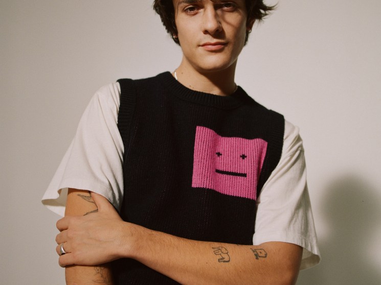 Portrait of French DJ Kungs wearing a black knit vest with pink face design over white t-shirt