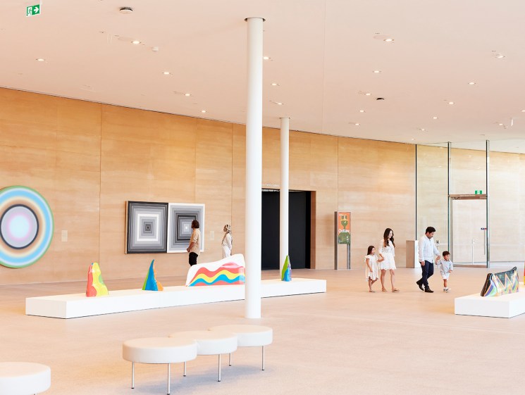 Modern gallery interior with colorful contemporary artworks on white platforms and visitors exploring the space