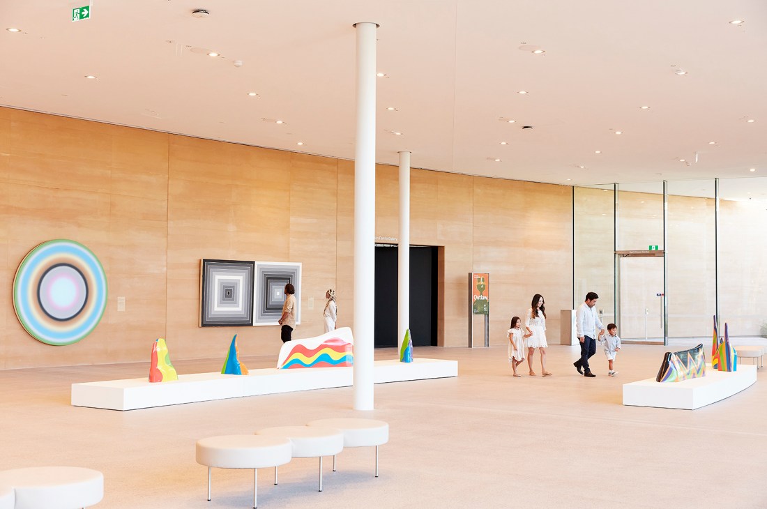 Modern gallery interior with colorful contemporary artworks on white platforms and visitors exploring the space