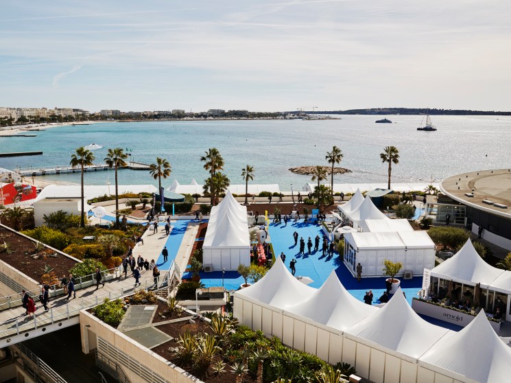 Aerial view of white exhibition tents and crowds at the Palais des Festivals et des Congrès in Cannes with bay in background