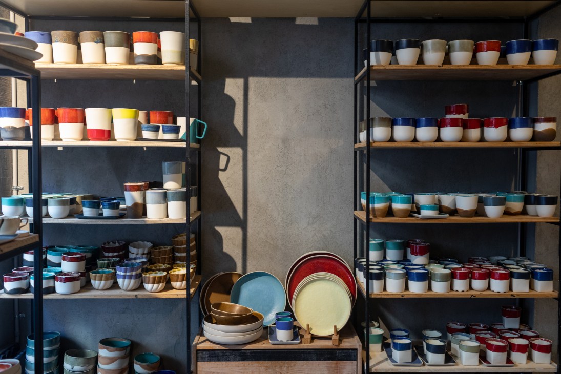 Colorful ceramic bowls and cups displayed on wooden shelves in a pottery shop