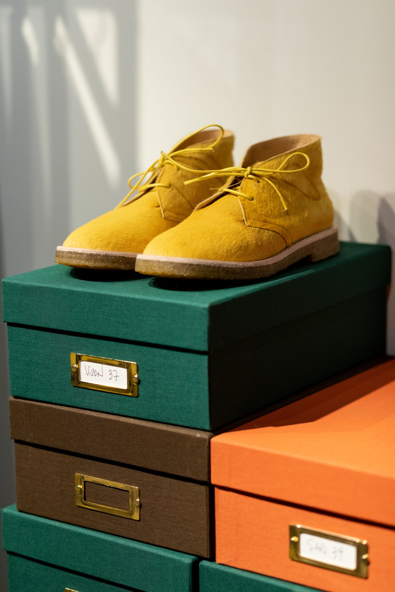 Yellow suede chukka boots with matching laces displayed on colorful stacked shoe boxes