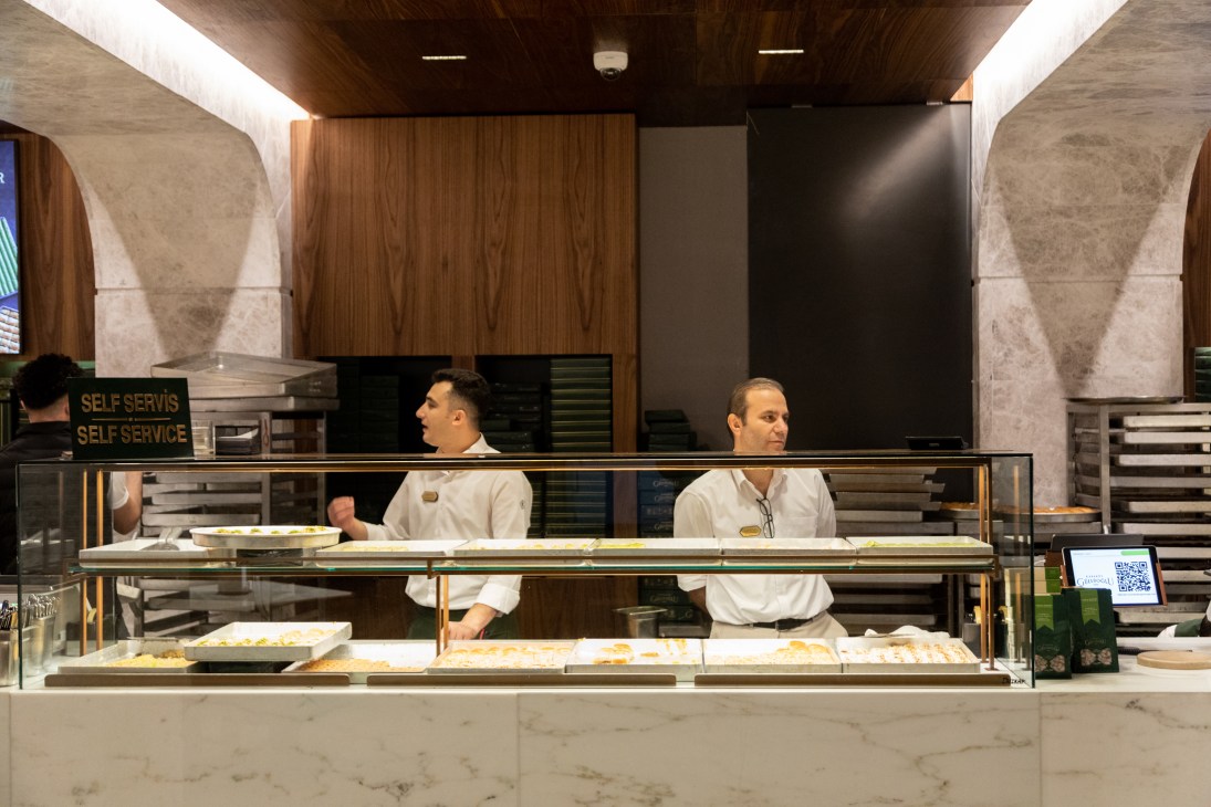 Pastry chefs in white uniforms working behind glass counter at Karakoy Gulluoglu baklava shop
