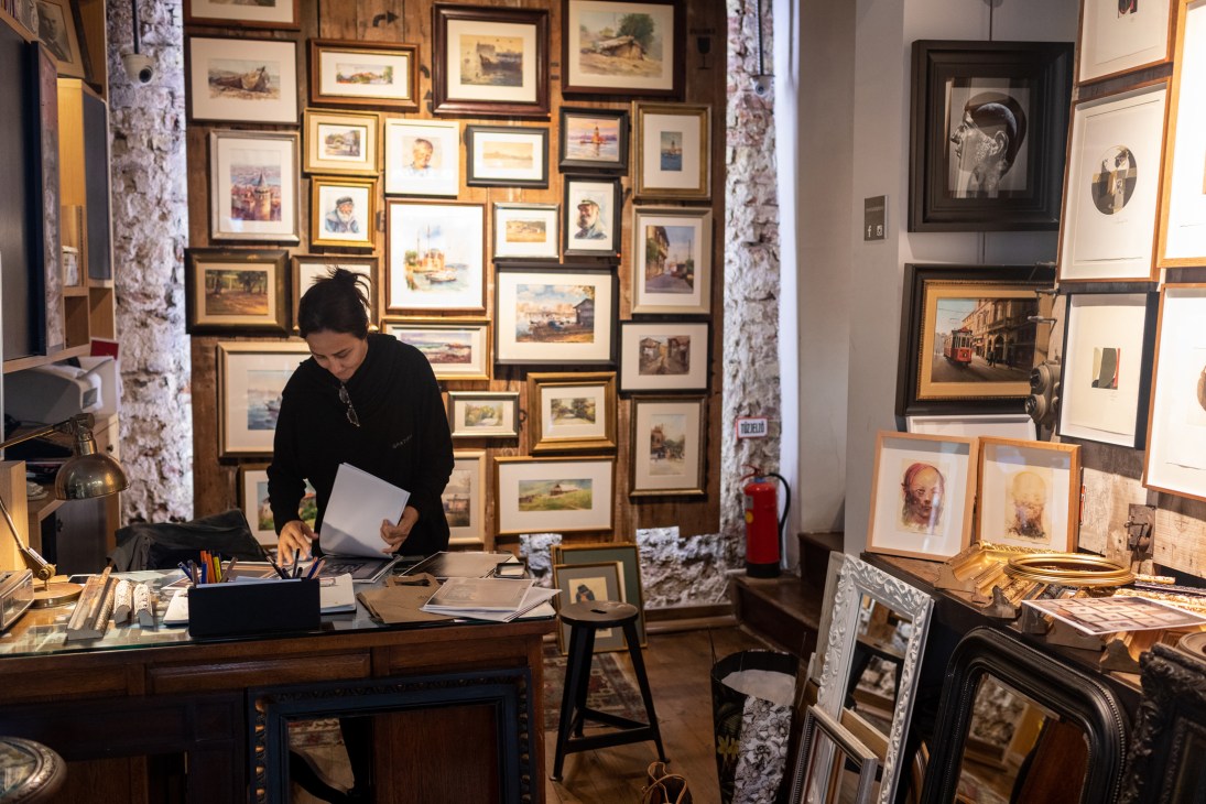 Woman examining artwork and framed pieces in an art gallery or framing shop with walls covered in paintings