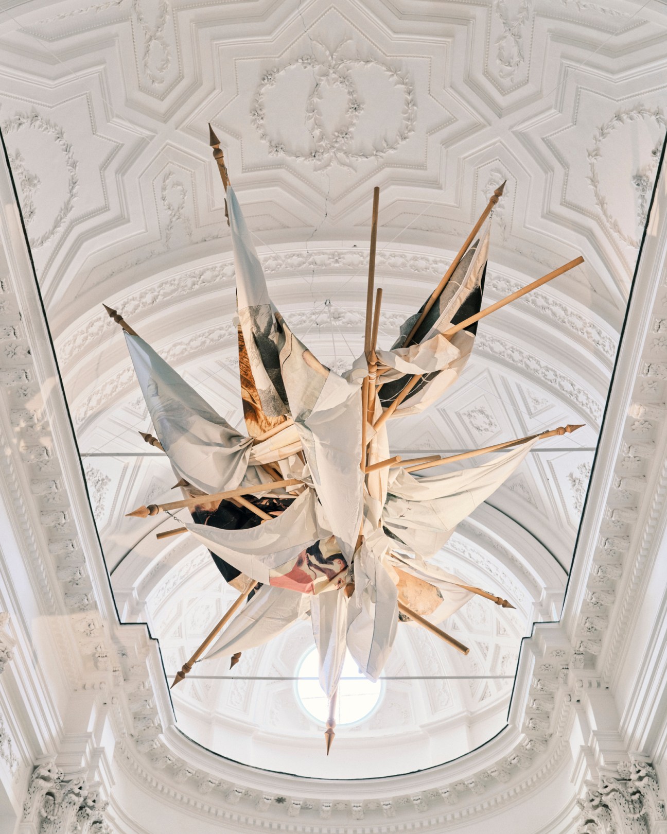 Giulio Paolini's colorful flags displayed against ornate white ceiling with geometric patterns