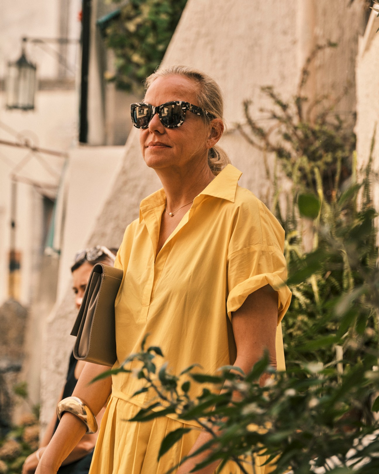 Woman in yellow shirt and sunglasses carrying a black bag while walking outdoors