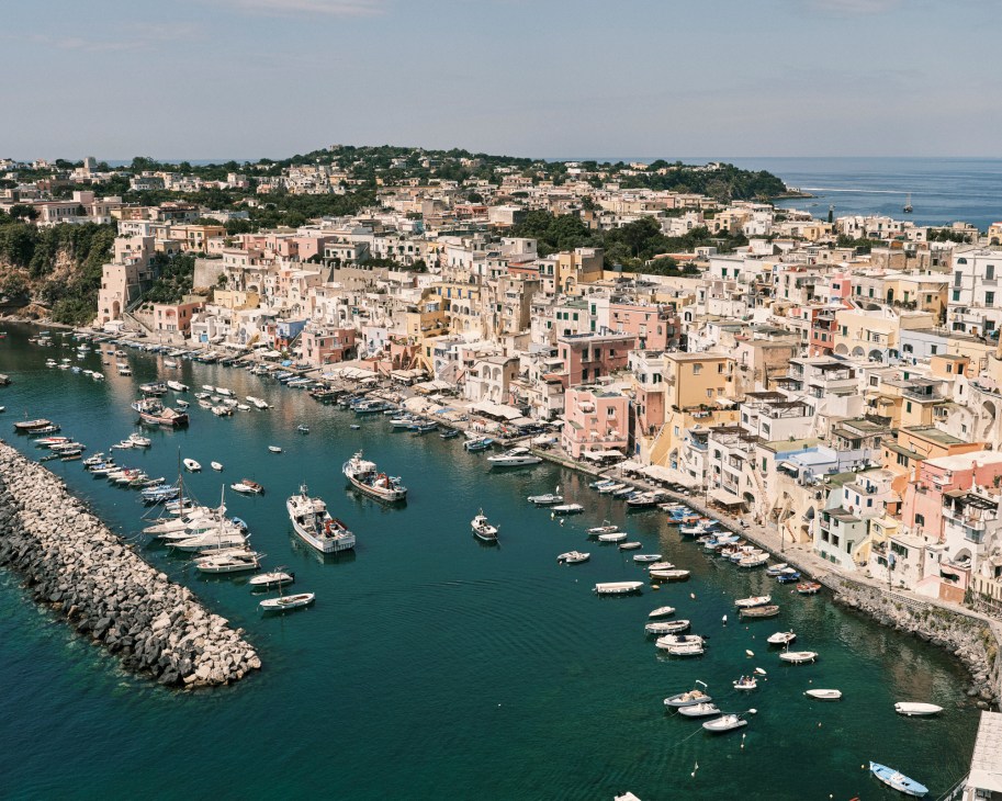 Aerial view of Procida's colorful waterfront houses and marina with boats in turquoise waters