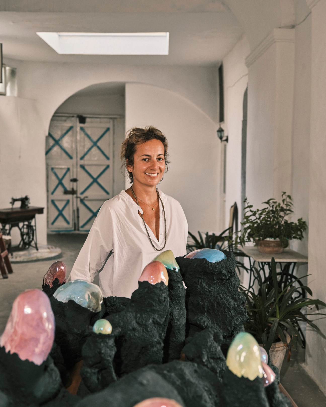 Gallery owner Federica Schiavo standing behind sculptural objects with iridescent surfaces in an interior space