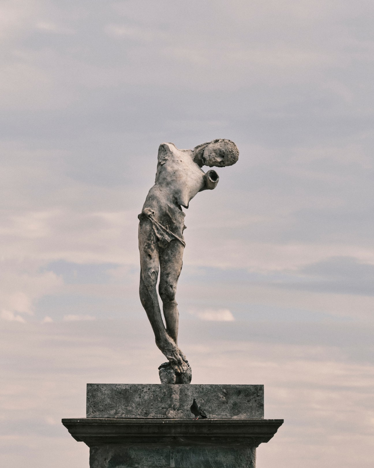 Classical marble statue of headless figure against cloudy sky on stone pedestal