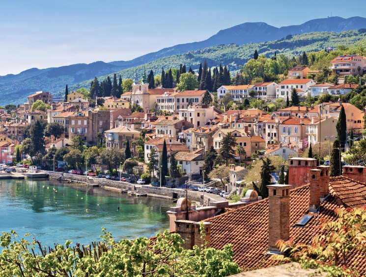 Colorful hillside Mediterranean town with terracotta roofs along turquoise water.