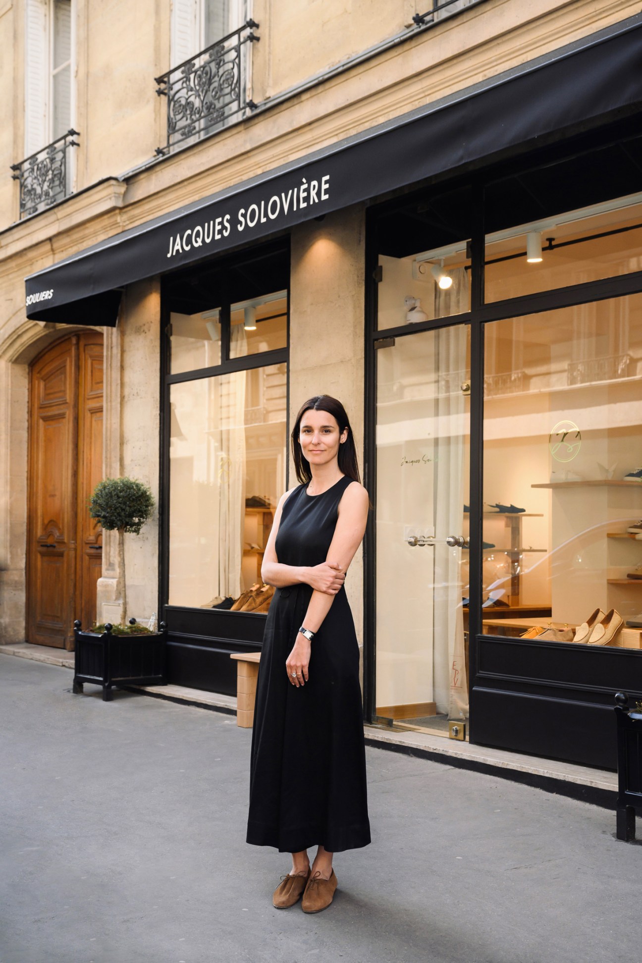 Woman in black dress standing outside Jacques Solovière Paris shoe boutique storefront