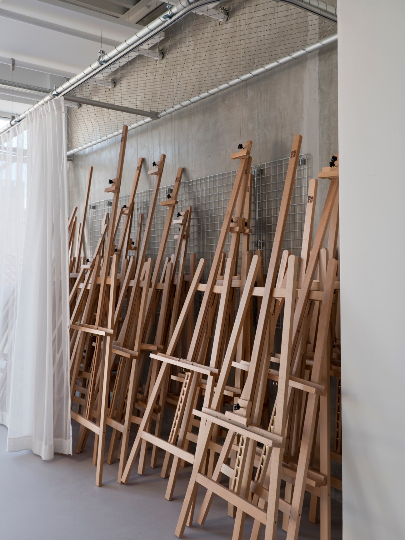 Wooden easels leaning against a wire mesh panel in a bright studio workspace.