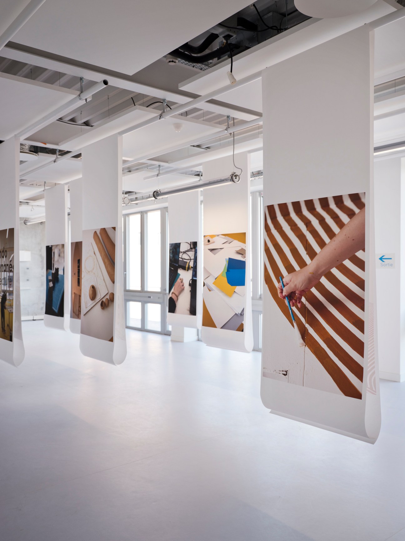 Minimalist white interior exhibition space with suspended hanging rails displaying design work and photographs.