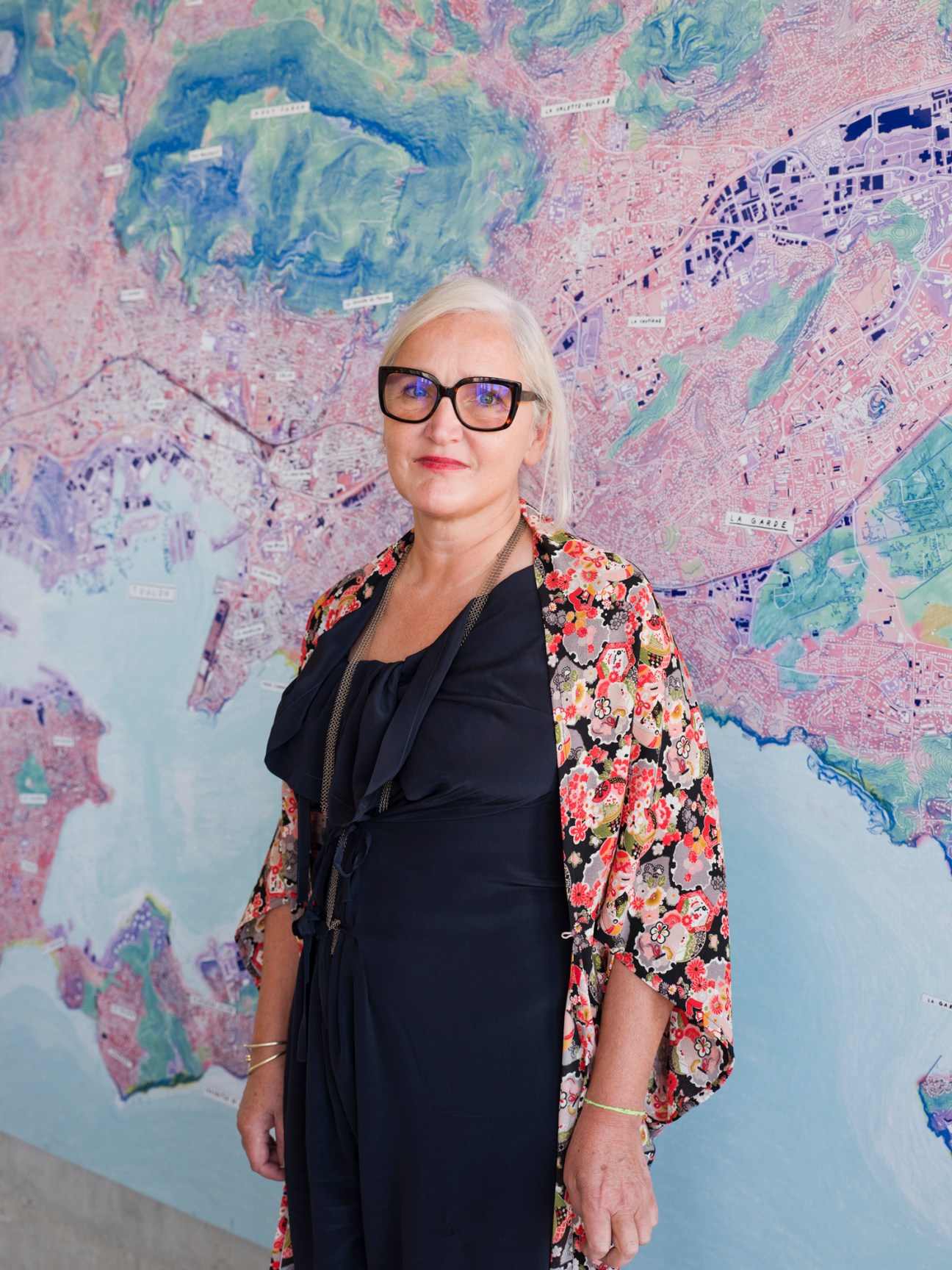 Margaret Iragui, director at Camondo Méditerranée design school in Toulon, France, standing in front of a colorful aerial map.