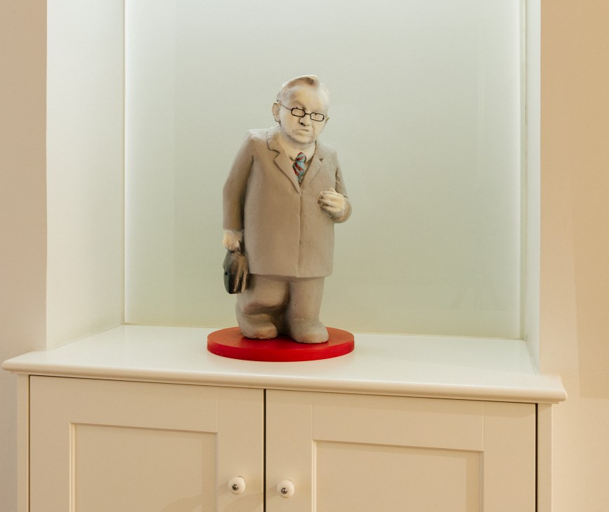 Figurine of man in beige suit and glasses on red base