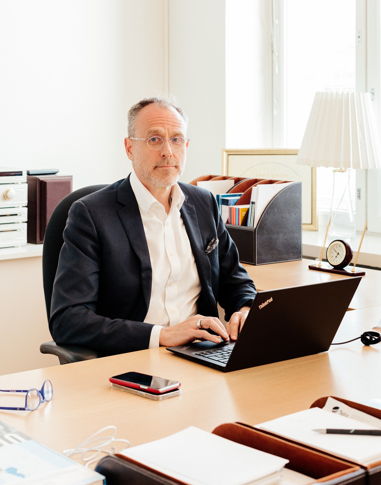 Janne Taalas in dark suit and glasses sitting at desk with laptop in Helsinki office